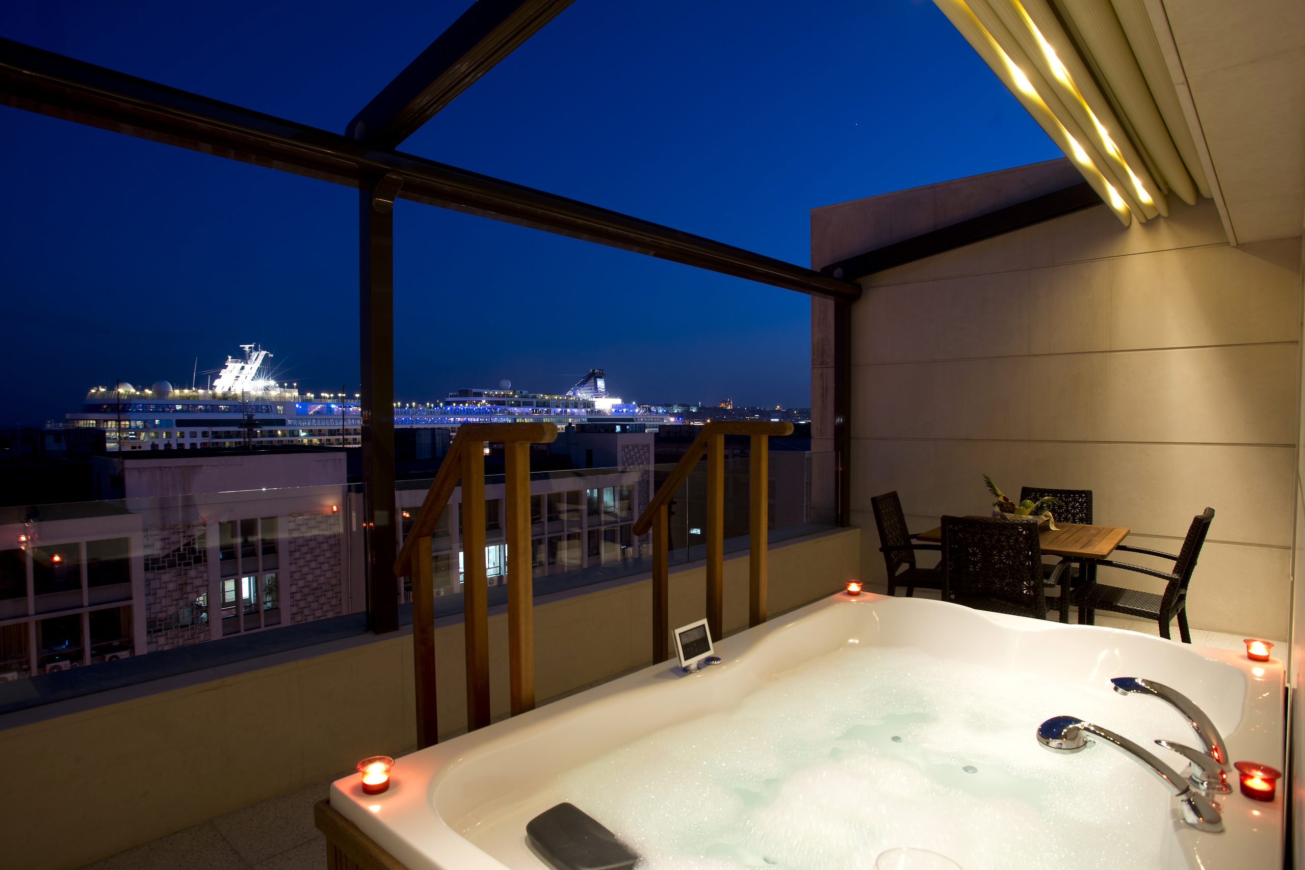 جاكوزي على شرفة Bosphorus Suite ليلًا، وخلفه سفينة سياحية في غلطة بورت